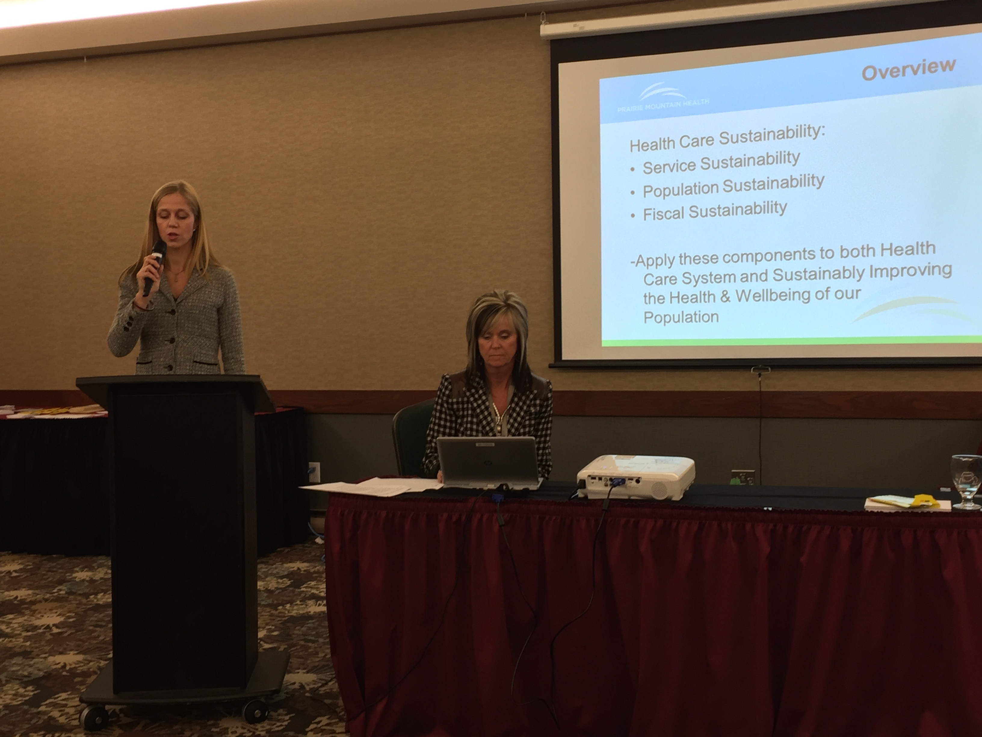 Penny Gilson sitting at a computer next to speaker Dr. Amy Frykoda at the PMH AGM